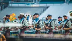 The drumline for the Music City Drum and Bugle Corps is in the middle of their show. They are positioned very close to one another, which means it's feasible for them to listen to one another.