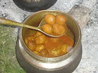A metal pot is filled with an orange-brown sauce and meatballs.
