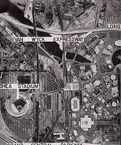 A black-and -white, aerial image of an urban area; visible are roads and buildings, a river, and labels saying "Shea Stadium", Van Wyck Expressway", and "Grand Central Parkway".