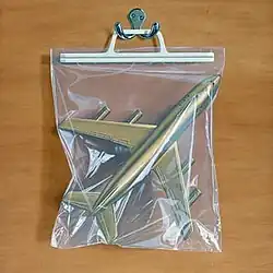A bag with a gold plane inside hanging from a hook on a wooden background