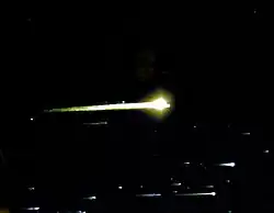 White streaks of light, with bright spots on the right side of them, fill the bottom of the frame. A larger yellow-tinted sphere with a streak is in the center of the frame. The background is black space.