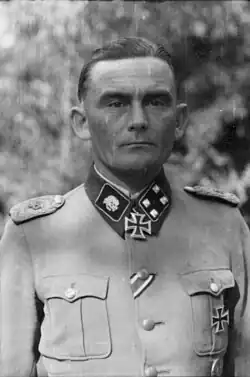 A black-and-white photograph of a man wearing a military uniform and neck order in shape of an Iron Cross. His hair is combed back and his facial expression is determined.