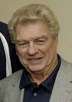 Headshot of a man smiling. He is wearing a checked coat with a blue shirt underneath.
