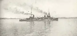 A large light gray ship passes slowly through calm waters.