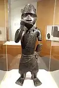 Figure of a horn blower; 1504–1550; copper alloy; 62.2 x 21.6 x 15.2 cm (241⁄2 x 81⁄2 x 6 in.); Brooklyn Museum (New York City). Blowing a horn or flute with his right hand, his left arm is truncated. He also wears a netted cap with chevron design decorated with a feather.