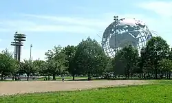 On a sunny summer day, a futuristic building and a huge sculpture representing Earth are visible behind trees and parkland.