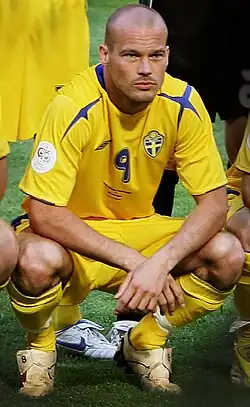 A soccer player in yellow shirt and yellow shorts squating for a photo.