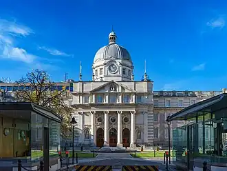 Building with central cupola and Ionic columns, with modern gatehouses in foreground