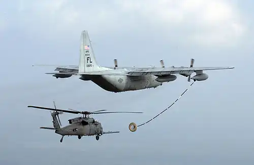 Helicopter with refuelling probe approaching the drogue trailed by a tanker.