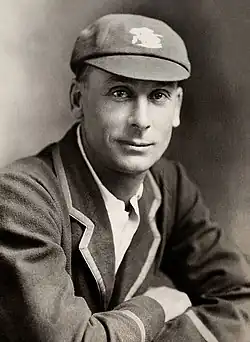 A black and white head and shoulders shot of a man wearing a cricket blazer and cap