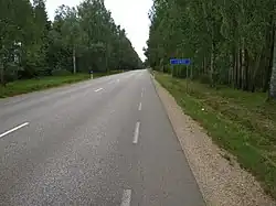 Picture of a road with trees lined on either side. There is a blue sign on the right side of the road that says “Londi”.