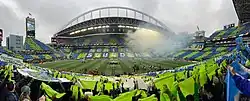 A view from inside the stadium during a tifo display with alternating blue and green cards held up by fans to form a checkerboard pattern in the seats
