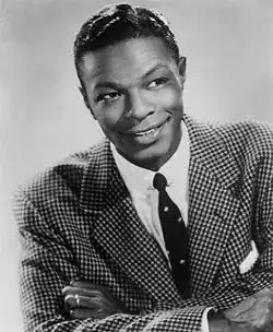 A black-and-white image of a man wearing a suit and looking towards the camera.