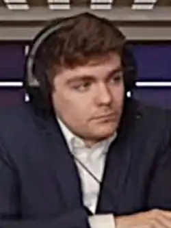 Webcam picture of Fuentes. He is wearing a white shirt, navy sport coat, and headphones.