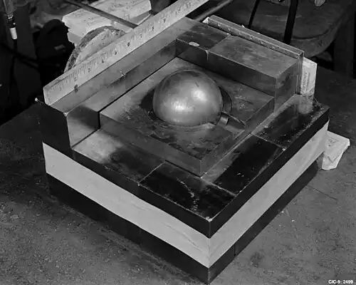 A square base of metal blocks, with a smaller square of metal on the top in the center, a Cooper block (the "core") contained in its center. A ruler along one side of the base shows roughly 10.5 inches (270 mm) square.