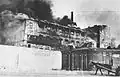 A factory razed by the SS burns during the suppression of the Warsaw ghetto uprising. Note identified by Yad Vashem as view from the Aryan side. Gliniana St. near the cemetery. On the left is Okopowa St. and at the front is the ghetto walls