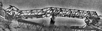 Wide, black and white view of Thanh Hóa Bridge badly damaged. The left support column has collapsed.