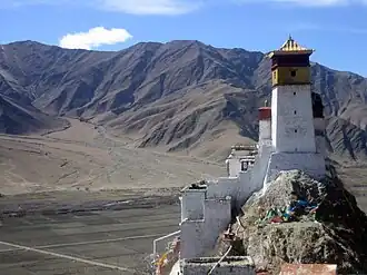 A palace in white stone with a yellow top overlooking a barren valley