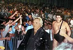 Bobby Heenan (front), a Caucasian man in a black sequin jacket, leads André the Giant to the ring (1989)